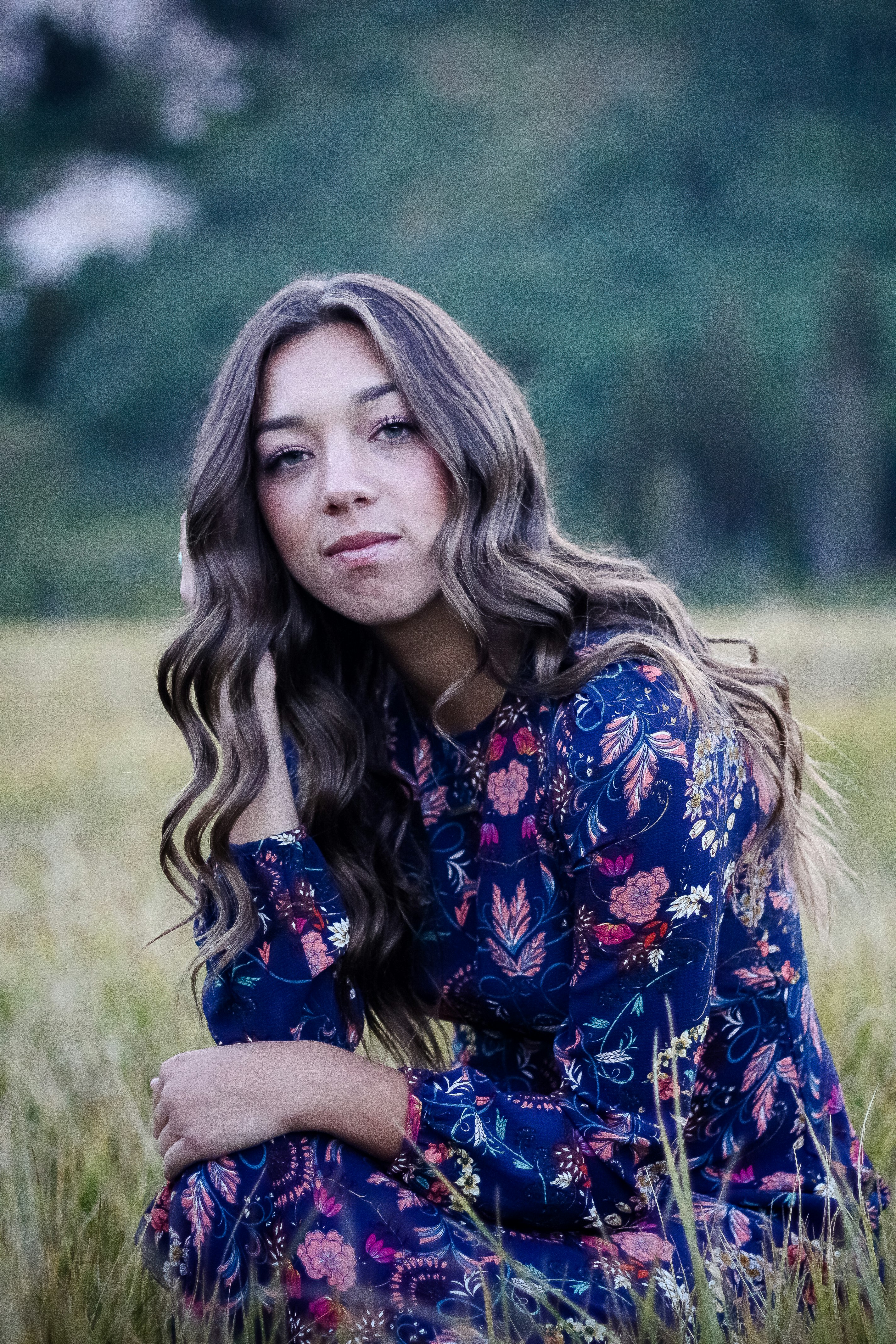 selective focus photo of woman sitting beside grass and wearing blue and white floral dress